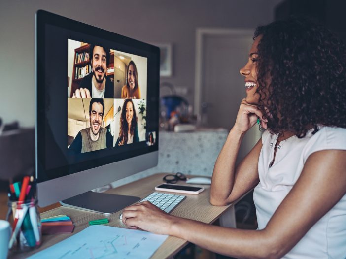 Woman smiling during a video call with four colleagues shown in a grid on her monitor